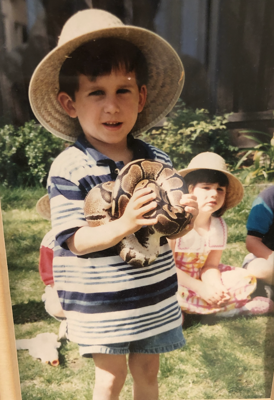 Me as a kid in a straw hat holding a ball python at a reptile-themed birthday party